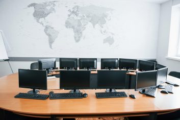 Business office at daytime with many computer screens. Map on the wall.